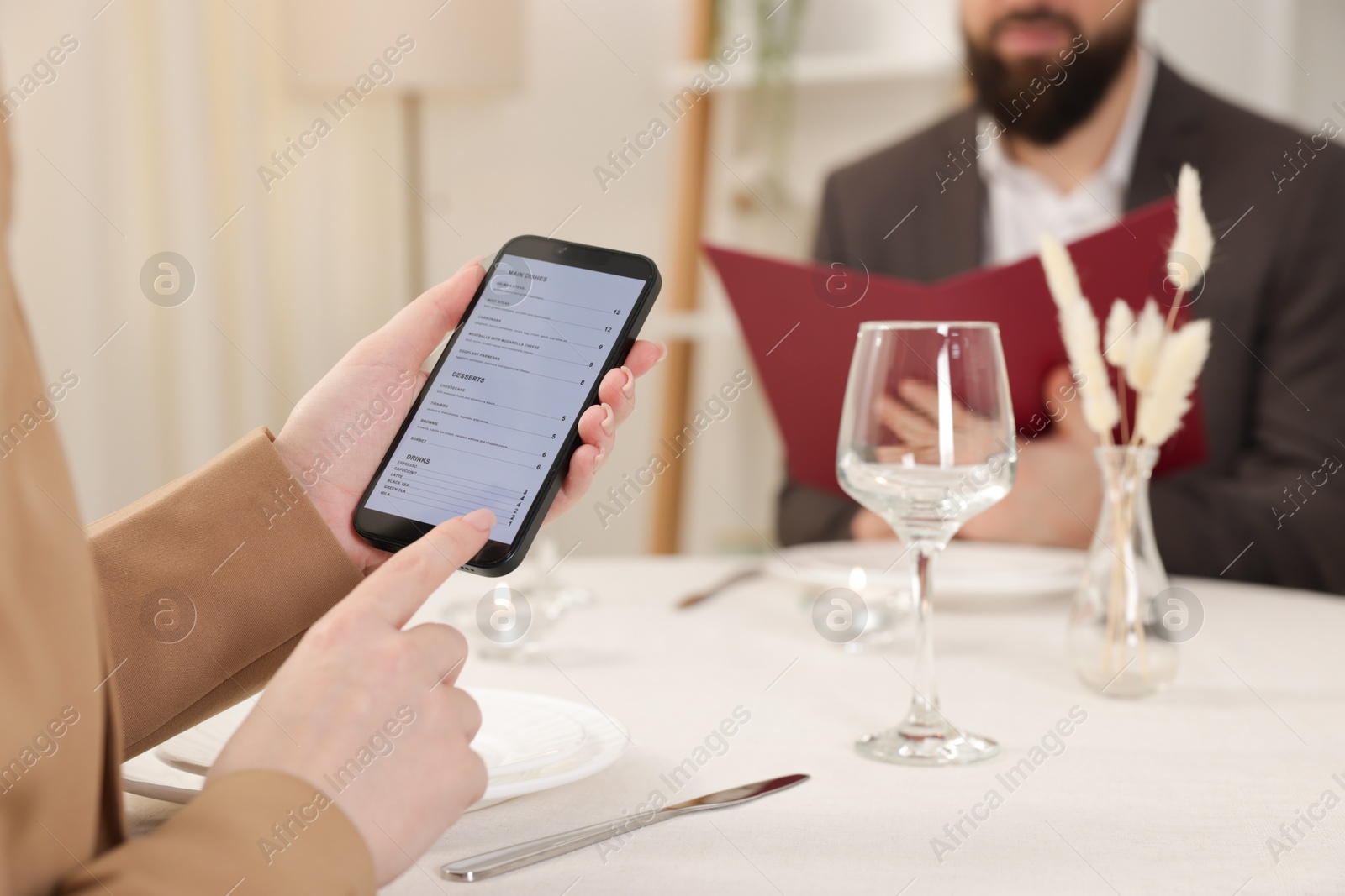 Photo of Woman viewing menu on smartphone at table in restaurant, closeup