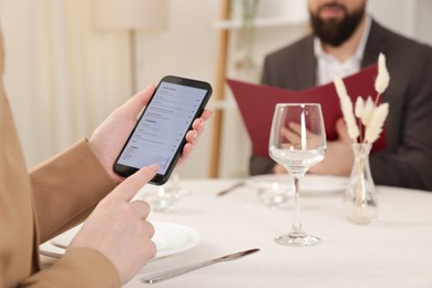 Photo of Woman viewing menu on smartphone at table in restaurant, closeup