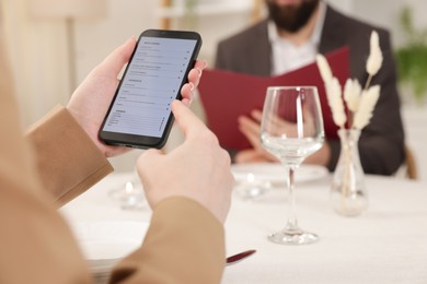 Photo of Woman viewing menu on smartphone at table in restaurant, closeup