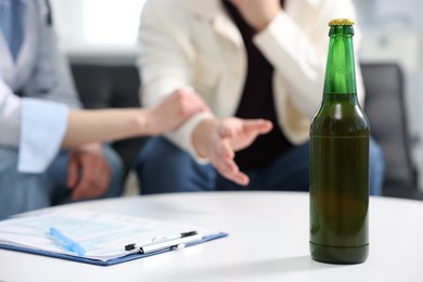 Photo of Alcoholic man having appointment with healthcare specialist in clinic, focus on bottle of beer. Addiction treatment