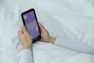 Photo of Menstruation. Woman using period calendar application on smartphone in bed indoors, closeup