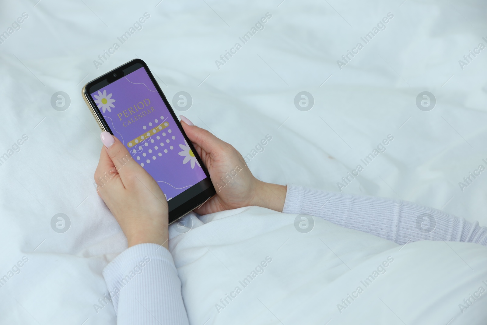 Photo of Menstruation. Woman using period calendar application on smartphone in bed indoors, closeup