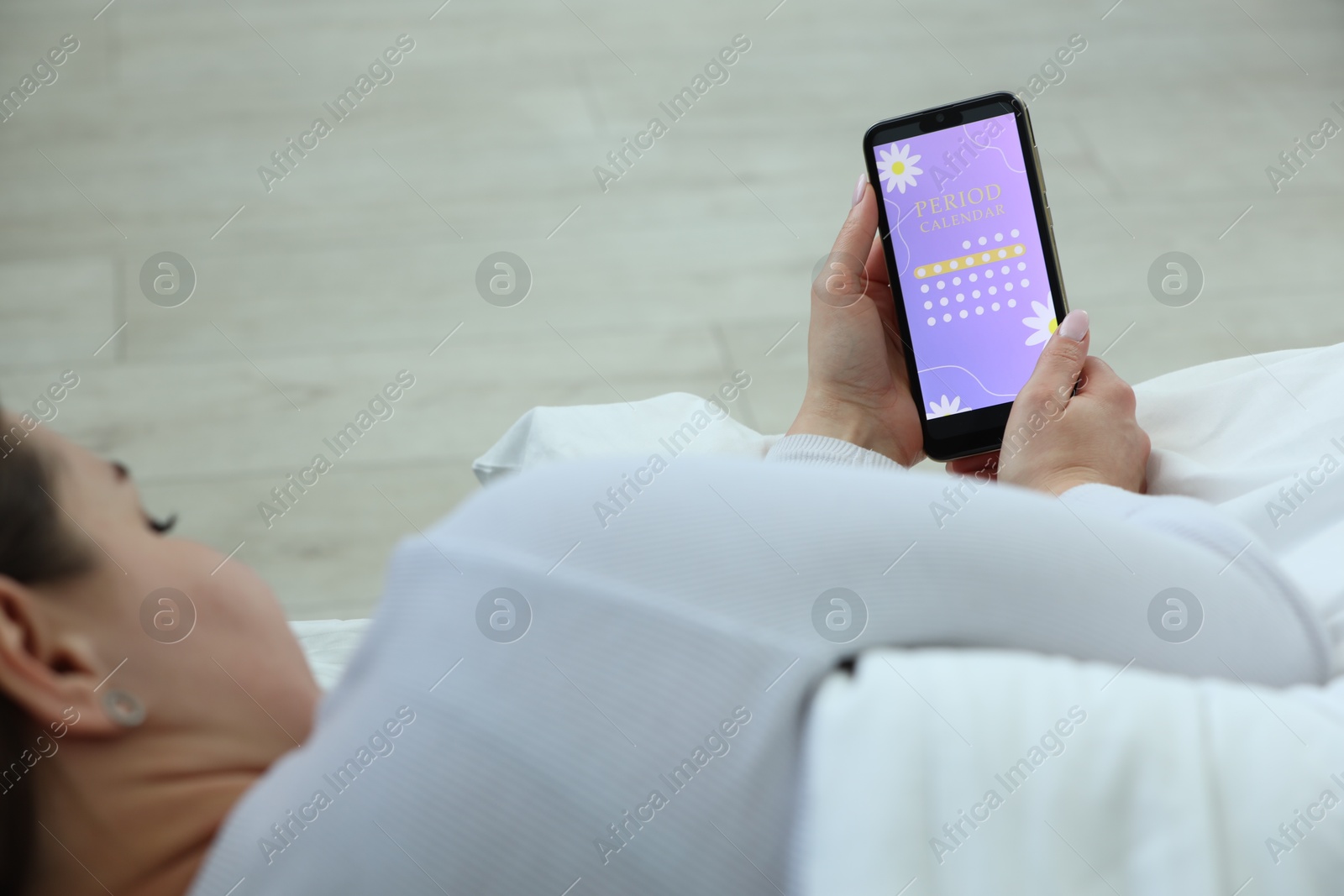 Photo of Menstruation. Woman using period calendar application on smartphone in bed indoors, closeup