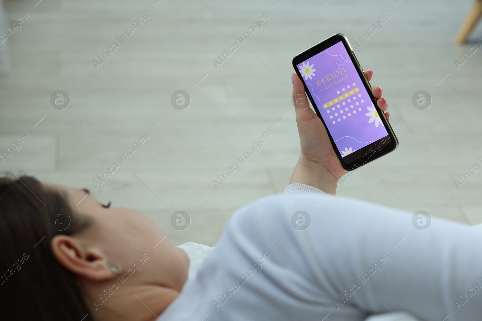 Photo of Menstruation. Woman using period calendar application on smartphone indoors