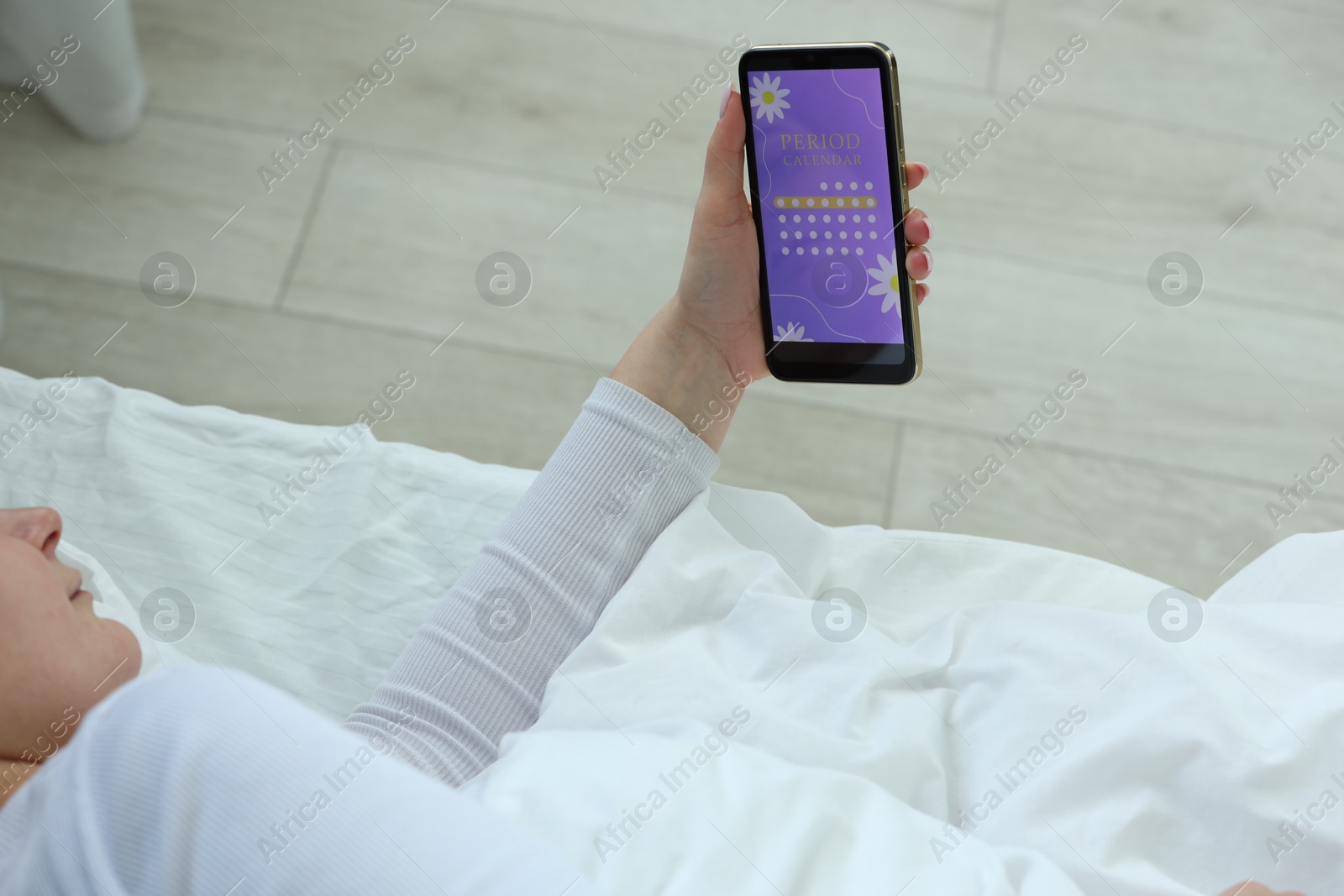 Photo of Menstruation. Woman using period calendar application on smartphone in bed indoors, above view