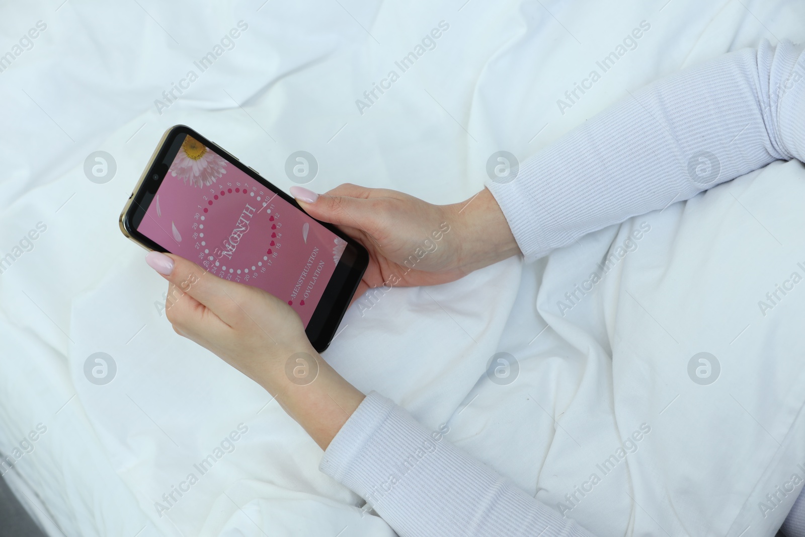 Photo of Menstruation. Woman using period calendar application on smartphone in bed indoors, above view