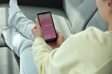 Photo of Menstruation. Woman using period calendar application on smartphone indoors, closeup