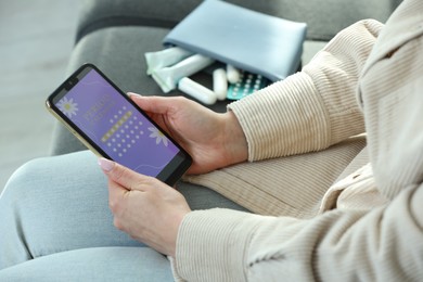 Photo of Menstruation. Woman using period calendar application on smartphone indoors, closeup