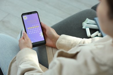 Photo of Menstruation. Woman using period calendar application on smartphone indoors, closeup