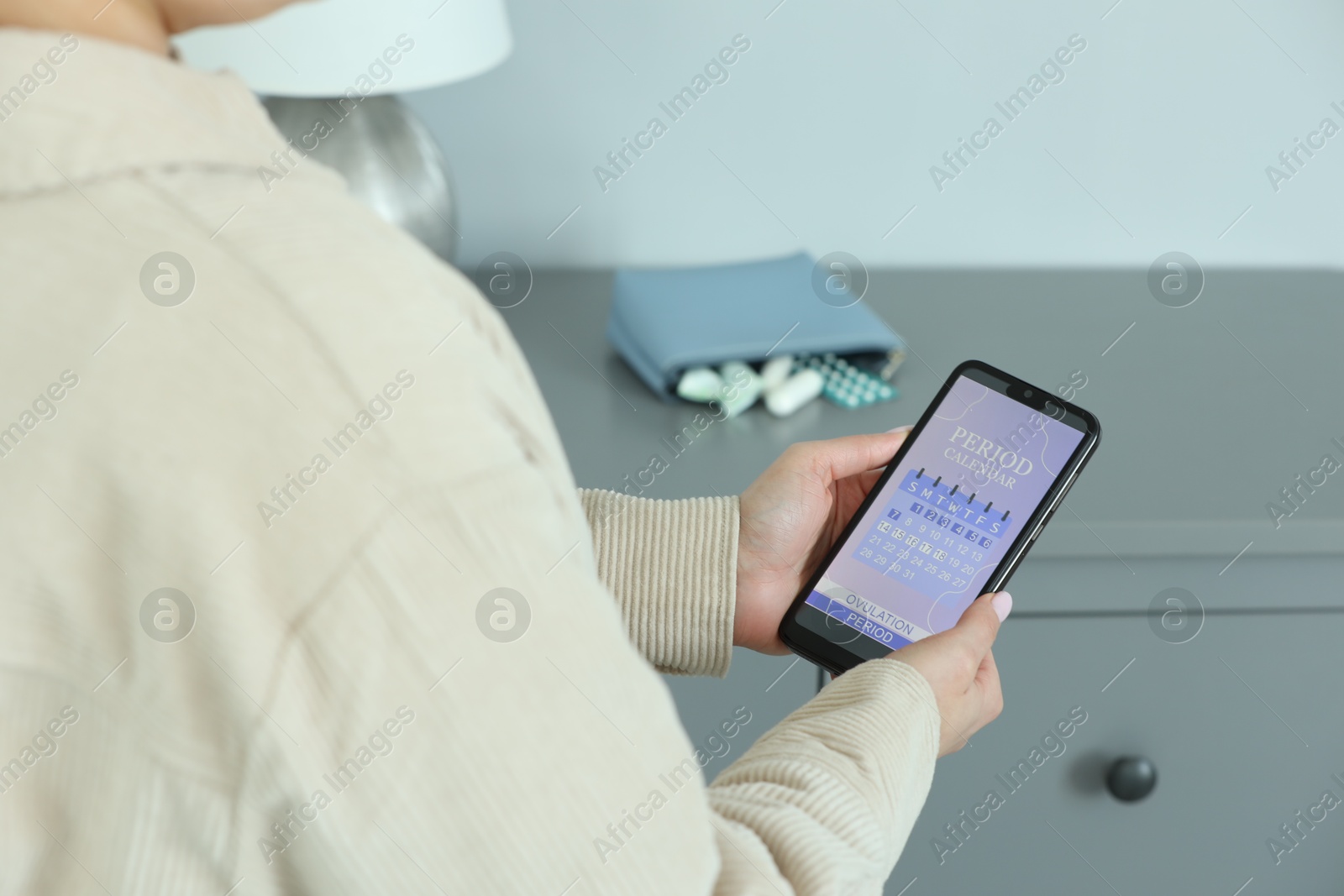 Photo of Menstruation. Woman using period calendar application on smartphone indoors, closeup