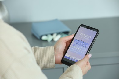 Photo of Menstruation. Woman using period calendar application on smartphone indoors, closeup