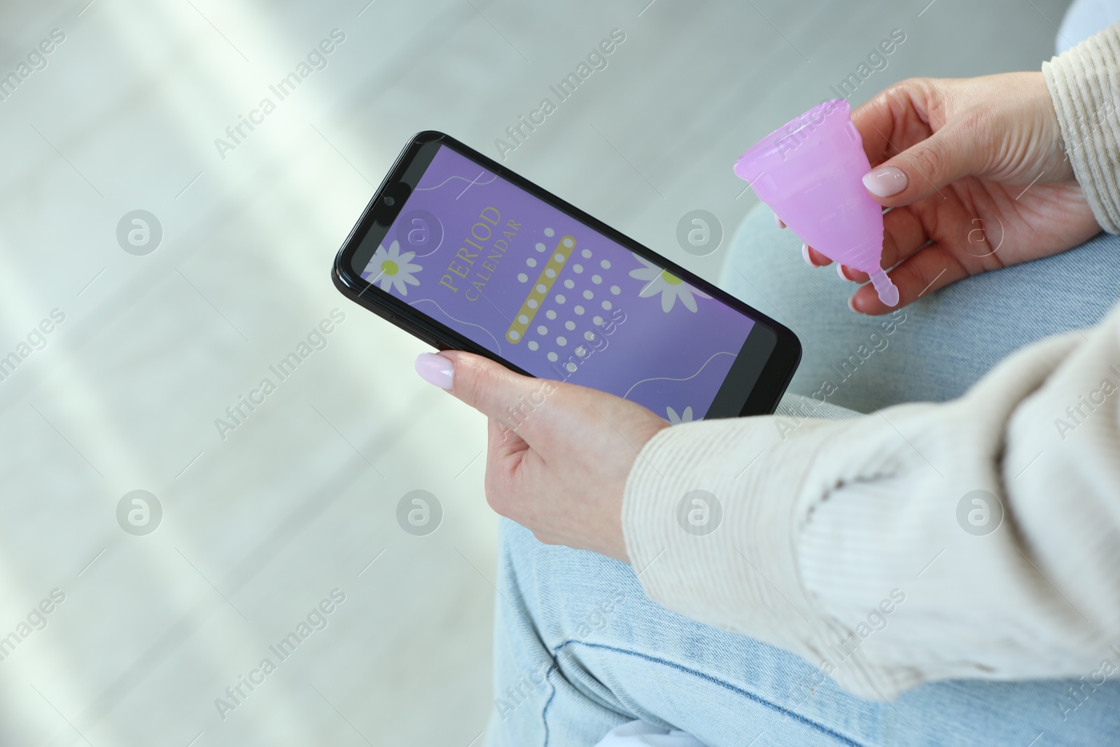 Photo of Menstruation. Woman with menstrual cup using period calendar application on smartphone indoors, closeup. Space for text