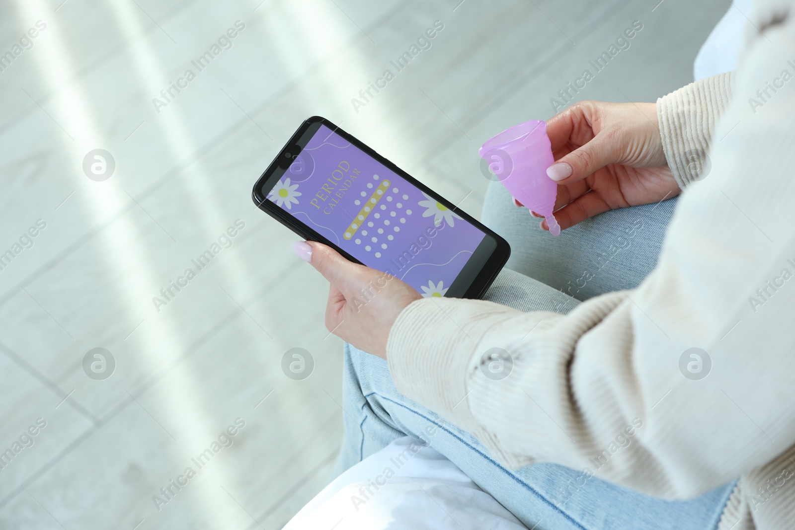 Photo of Menstruation. Woman with menstrual cup using period calendar application on smartphone indoors, closeup. Space for text