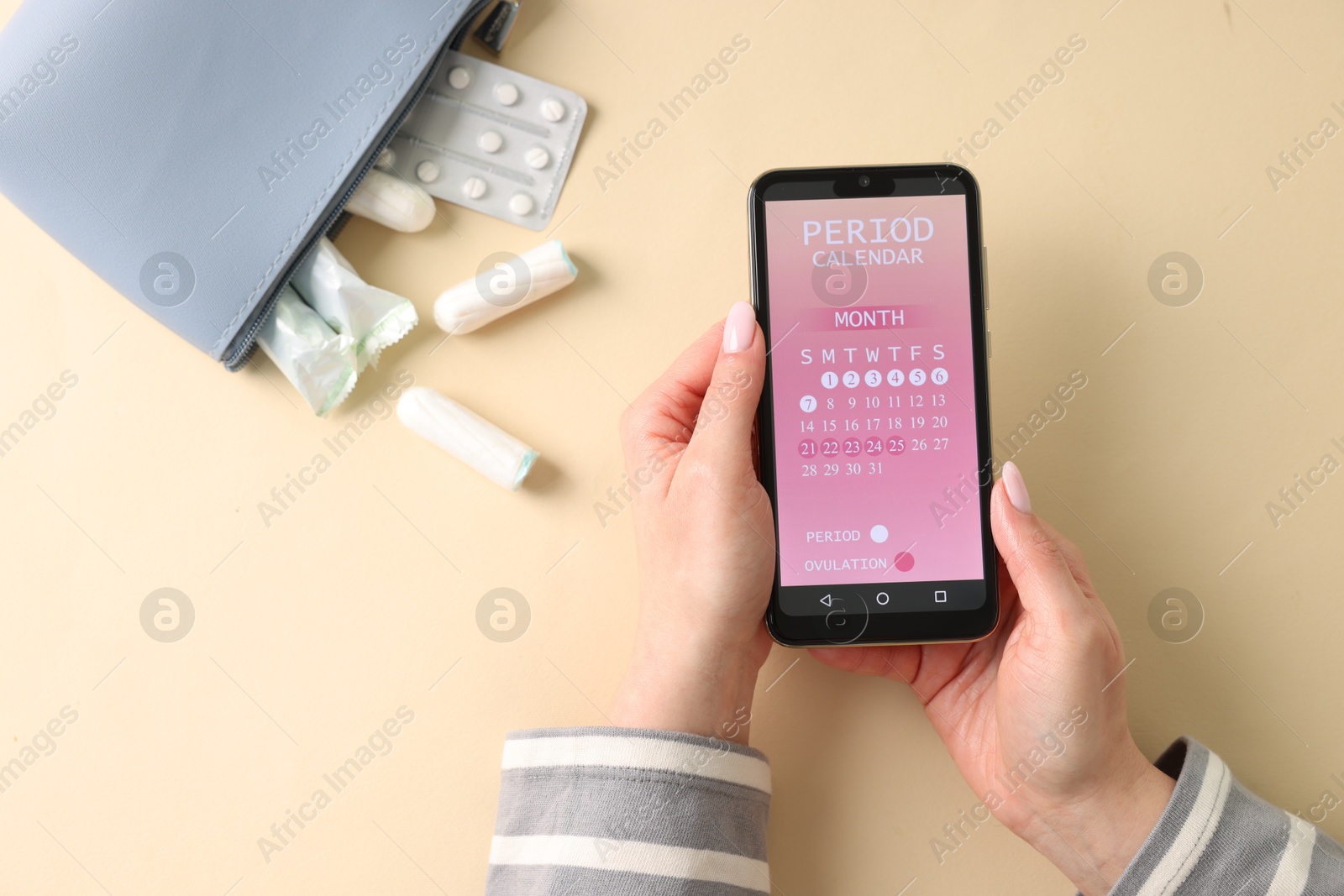 Photo of Menstruation. Woman holding smartphone with period calendar application on beige background, top view