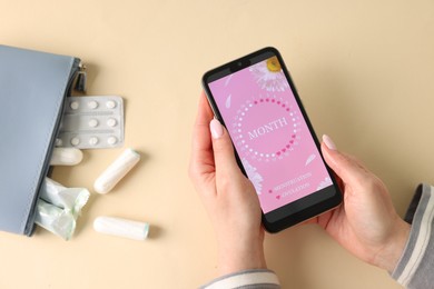 Photo of Menstruation. Woman holding smartphone with period calendar application on beige background, top view