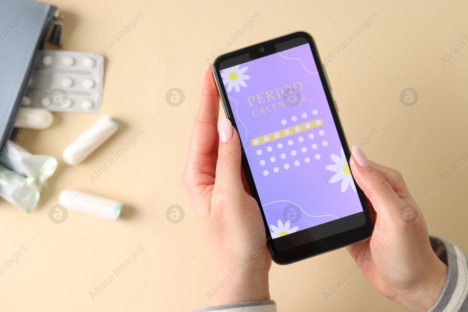 Photo of Menstruation. Woman holding smartphone with period calendar application on beige background, top view