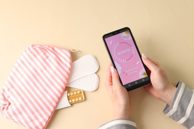 Photo of Menstruation. Woman holding smartphone with period calendar application on beige background, top view