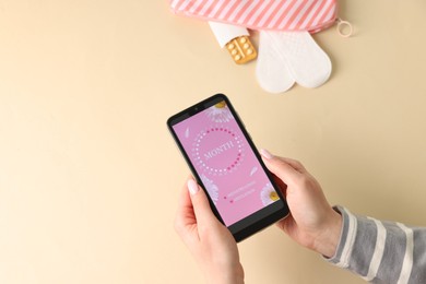 Photo of Menstruation. Woman holding smartphone with period calendar application on beige background, top view. Space for text