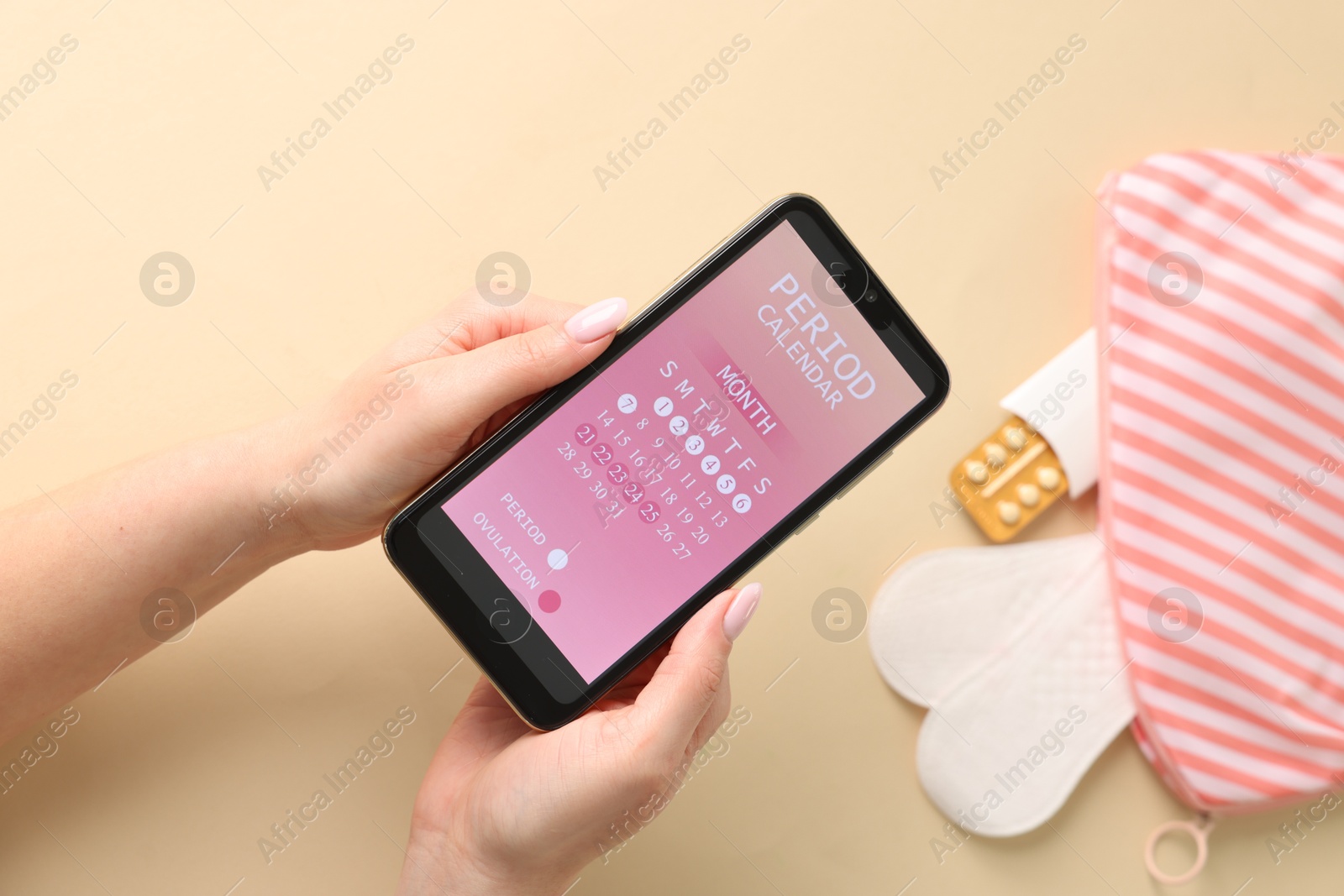 Photo of Menstruation. Woman holding smartphone with period calendar application on beige background, top view