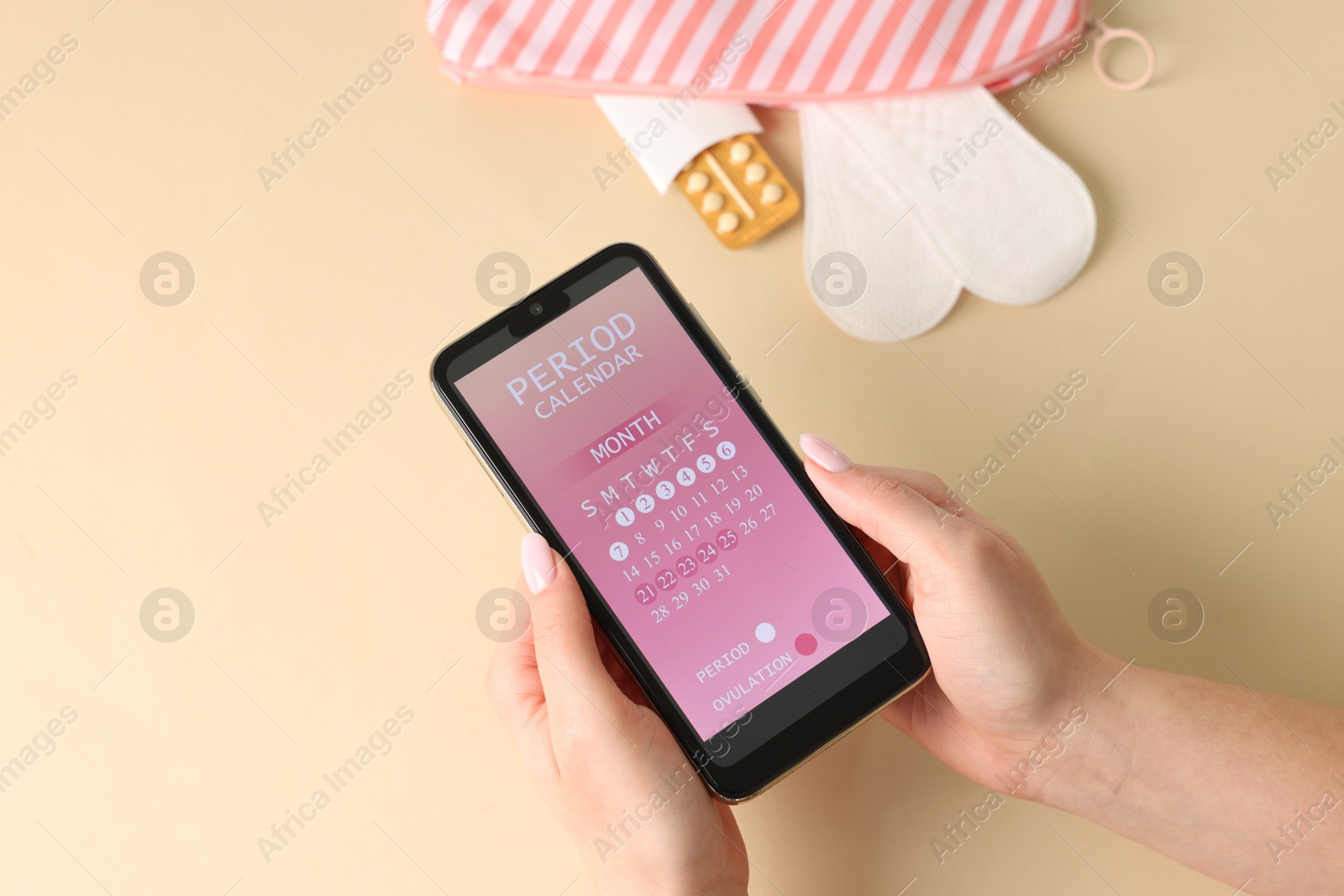 Photo of Menstruation. Woman holding smartphone with period calendar application on beige background, top view