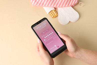 Photo of Menstruation. Woman holding smartphone with period calendar application on beige background, top view