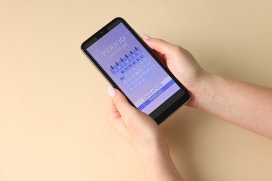 Photo of Menstruation. Woman holding smartphone with period calendar application on beige background, above view. Space for text