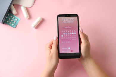 Photo of Menstruation. Woman holding smartphone with period calendar application on pink background, top view