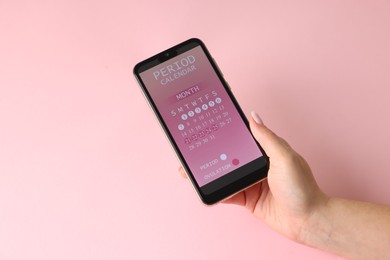 Photo of Menstruation. Woman holding smartphone with period calendar application on pink background, above view