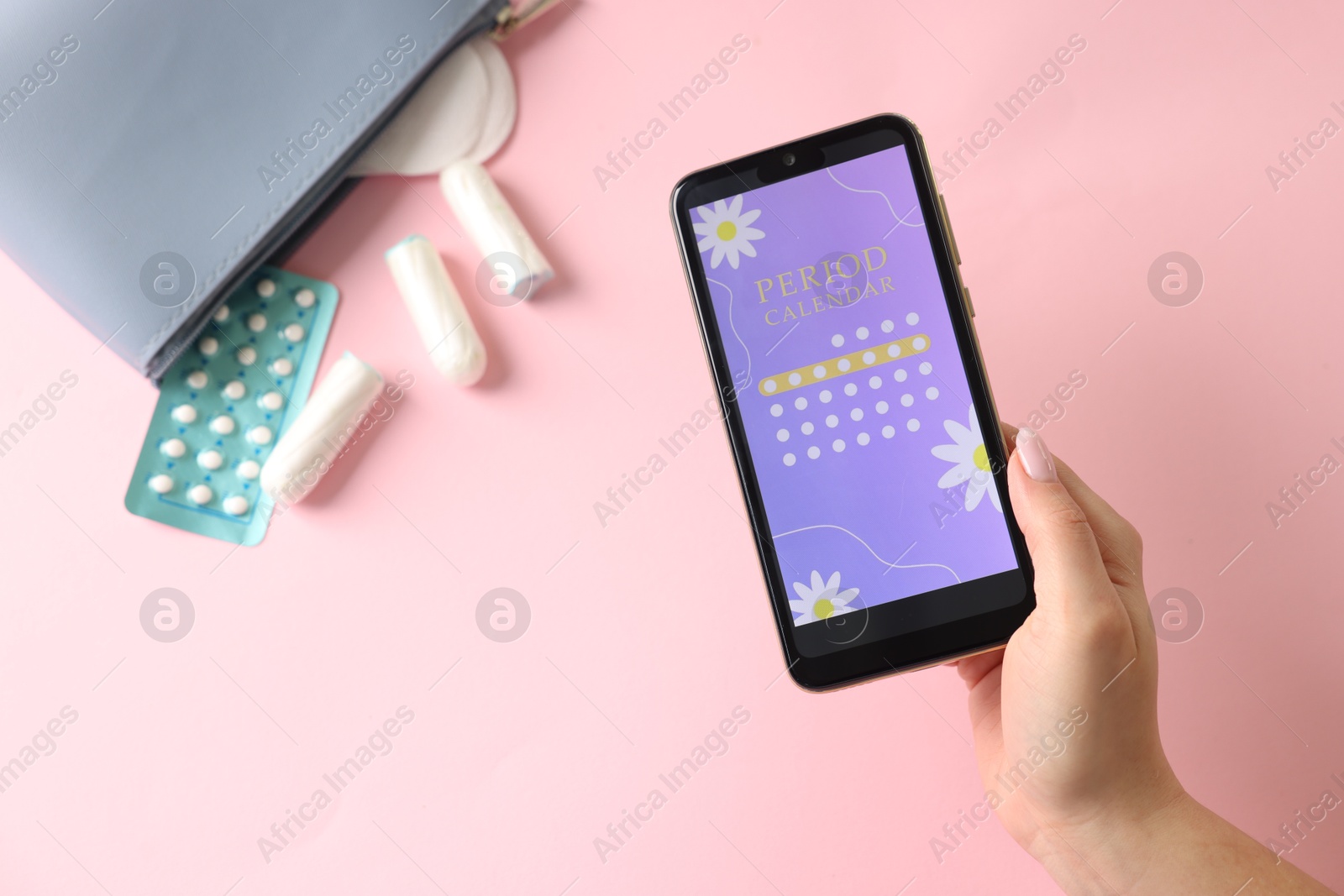 Photo of Menstruation. Woman holding smartphone with period calendar application on pink background, top view