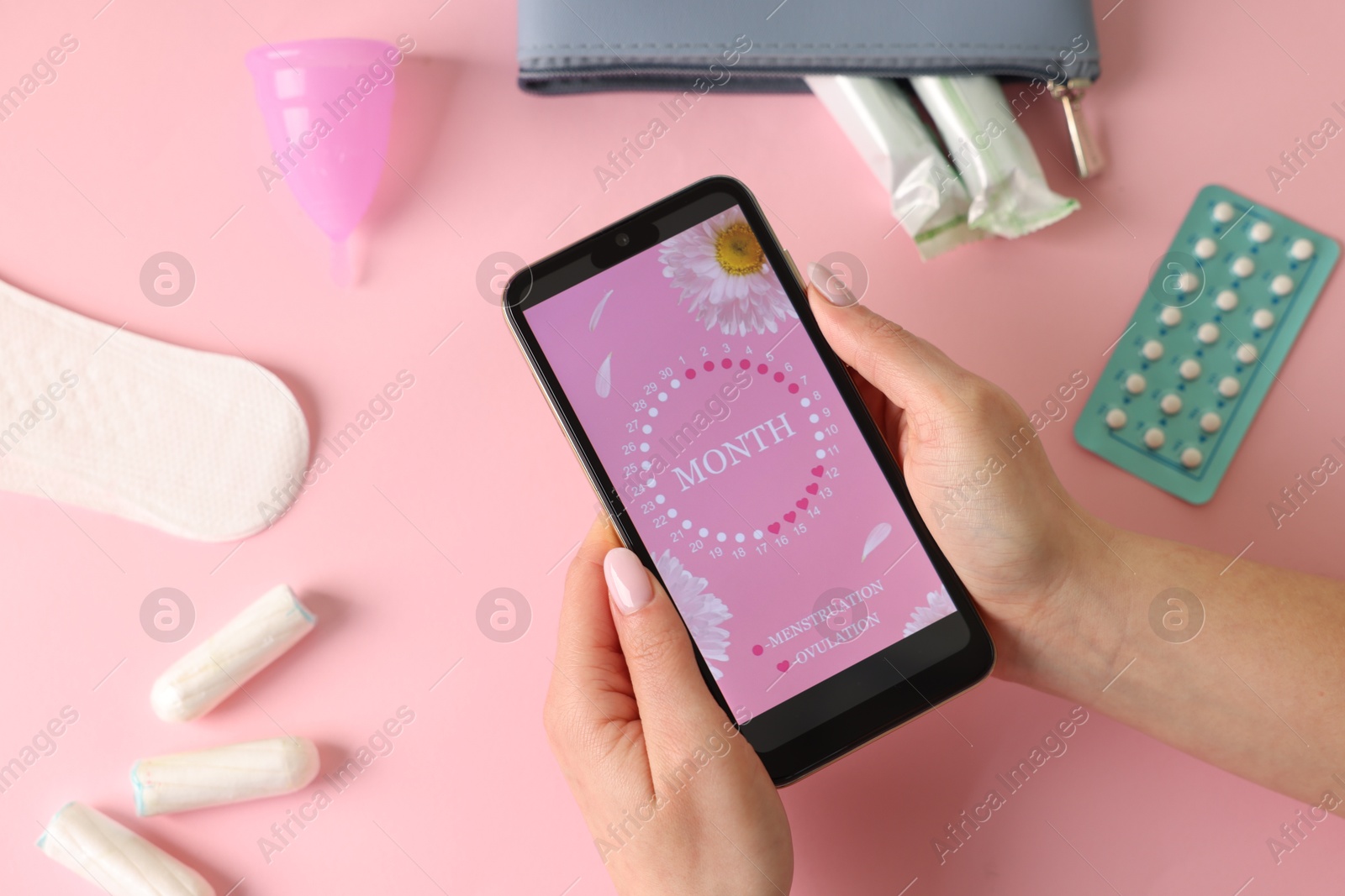 Photo of Menstruation. Woman holding smartphone with period calendar application on pink background, top view