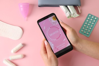 Photo of Menstruation. Woman holding smartphone with period calendar application on pink background, top view