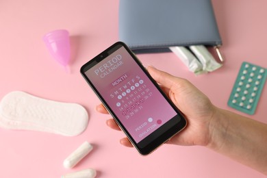 Photo of Menstruation. Woman holding smartphone with period calendar application on pink background, top view