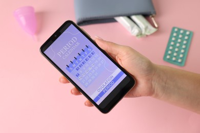 Photo of Menstruation. Woman holding smartphone with period calendar application on pink background, above view