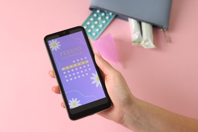 Photo of Menstruation. Woman holding smartphone with period calendar application on pink background, above view