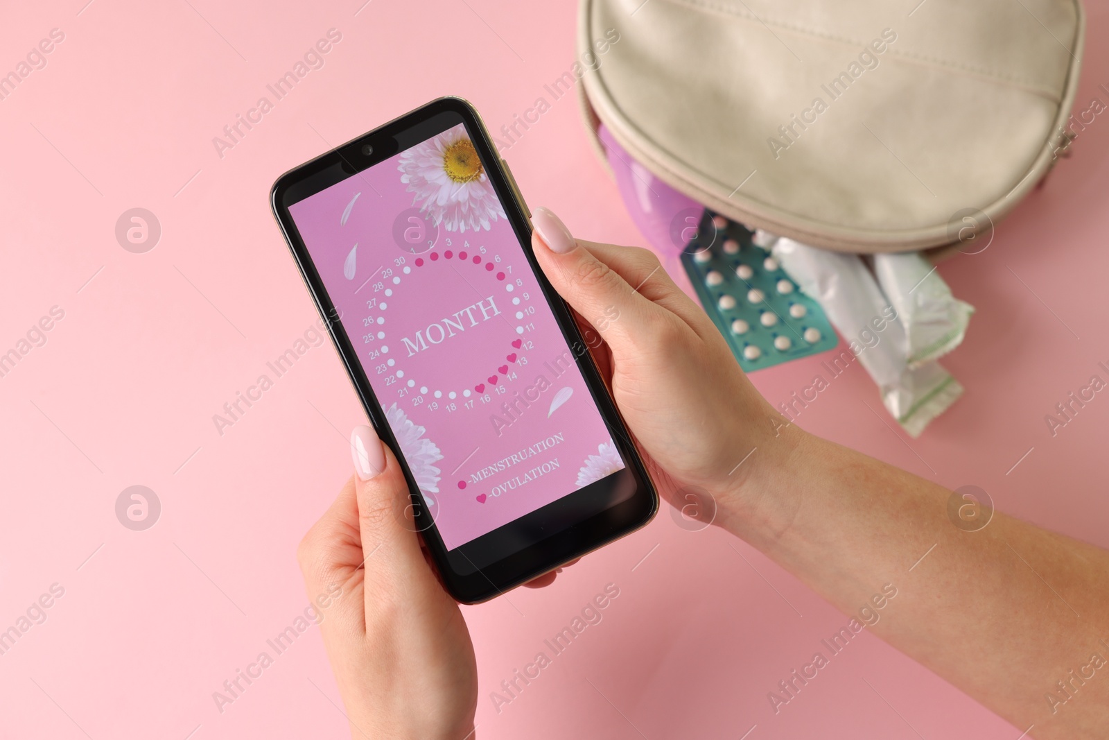 Photo of Menstruation. Woman holding smartphone with period calendar application on pink background, top view