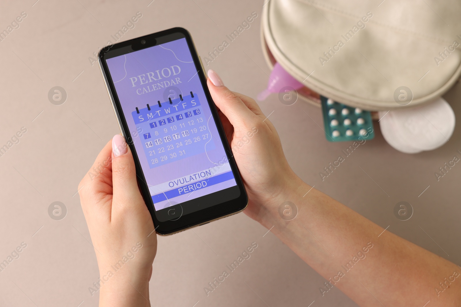 Photo of Menstruation. Woman holding smartphone with period calendar application on beige background, top view