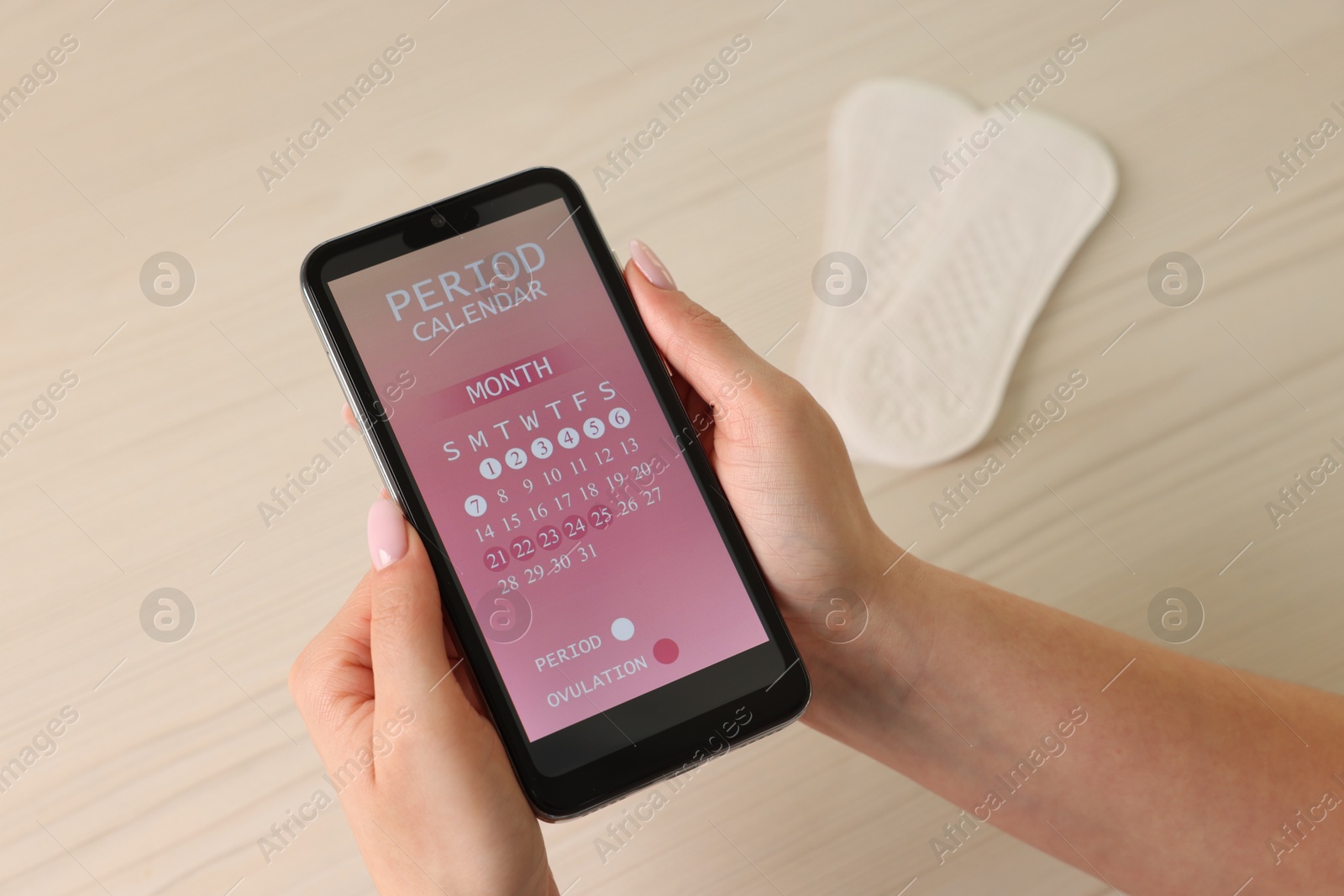 Photo of Menstruation. Woman using period calendar application on smartphone at wooden table, above view