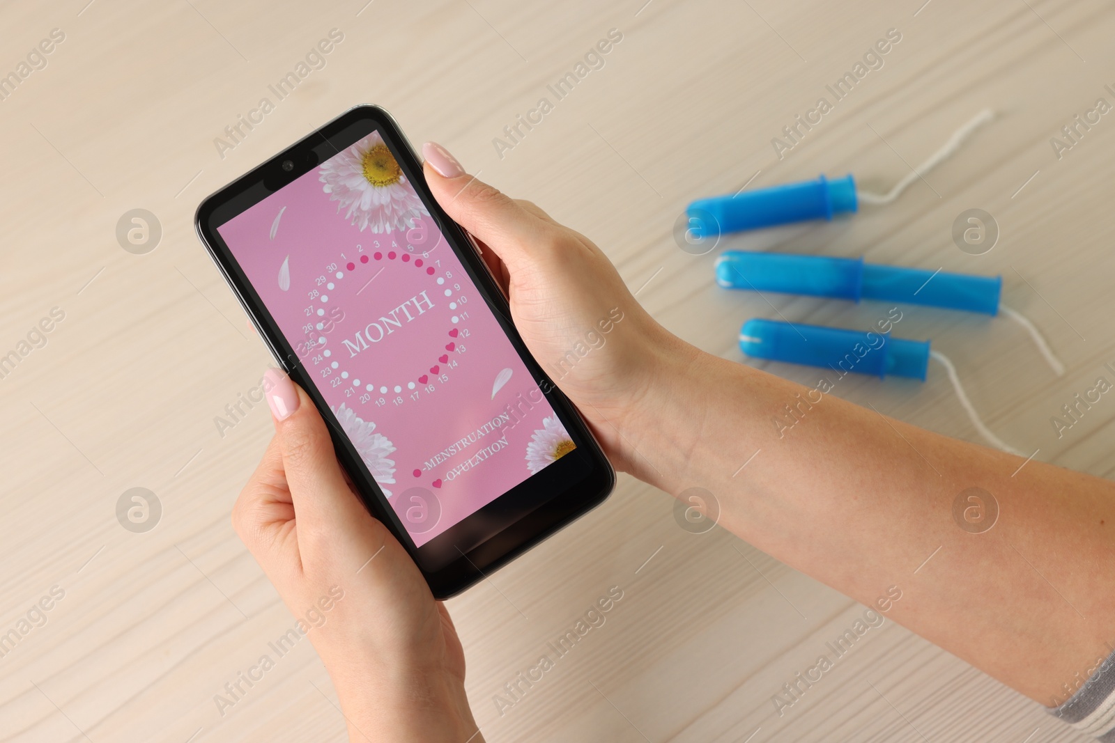 Photo of Menstruation. Woman using period calendar application on smartphone at wooden table, above view