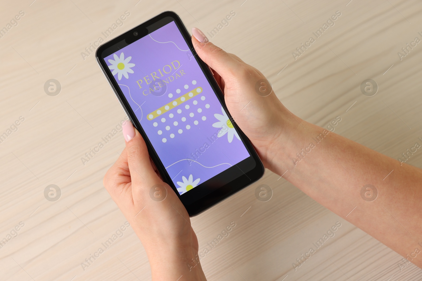 Photo of Menstruation. Woman using period calendar application on smartphone at wooden table, above view