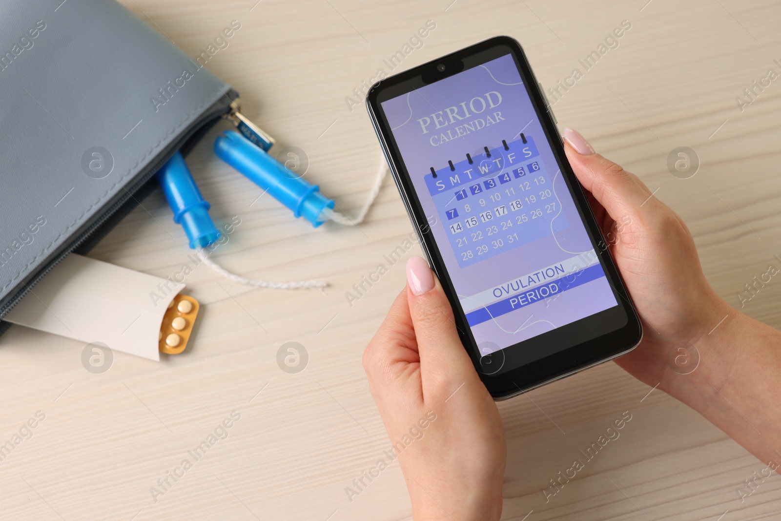 Photo of Menstruation. Woman using period calendar application on smartphone at wooden table, above view