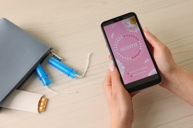 Photo of Menstruation. Woman using period calendar application on smartphone at wooden table, above view