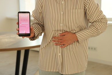 Photo of Menstruation. Woman holding smartphone with period calendar application and suffering from abdominal pain indoors, closeup