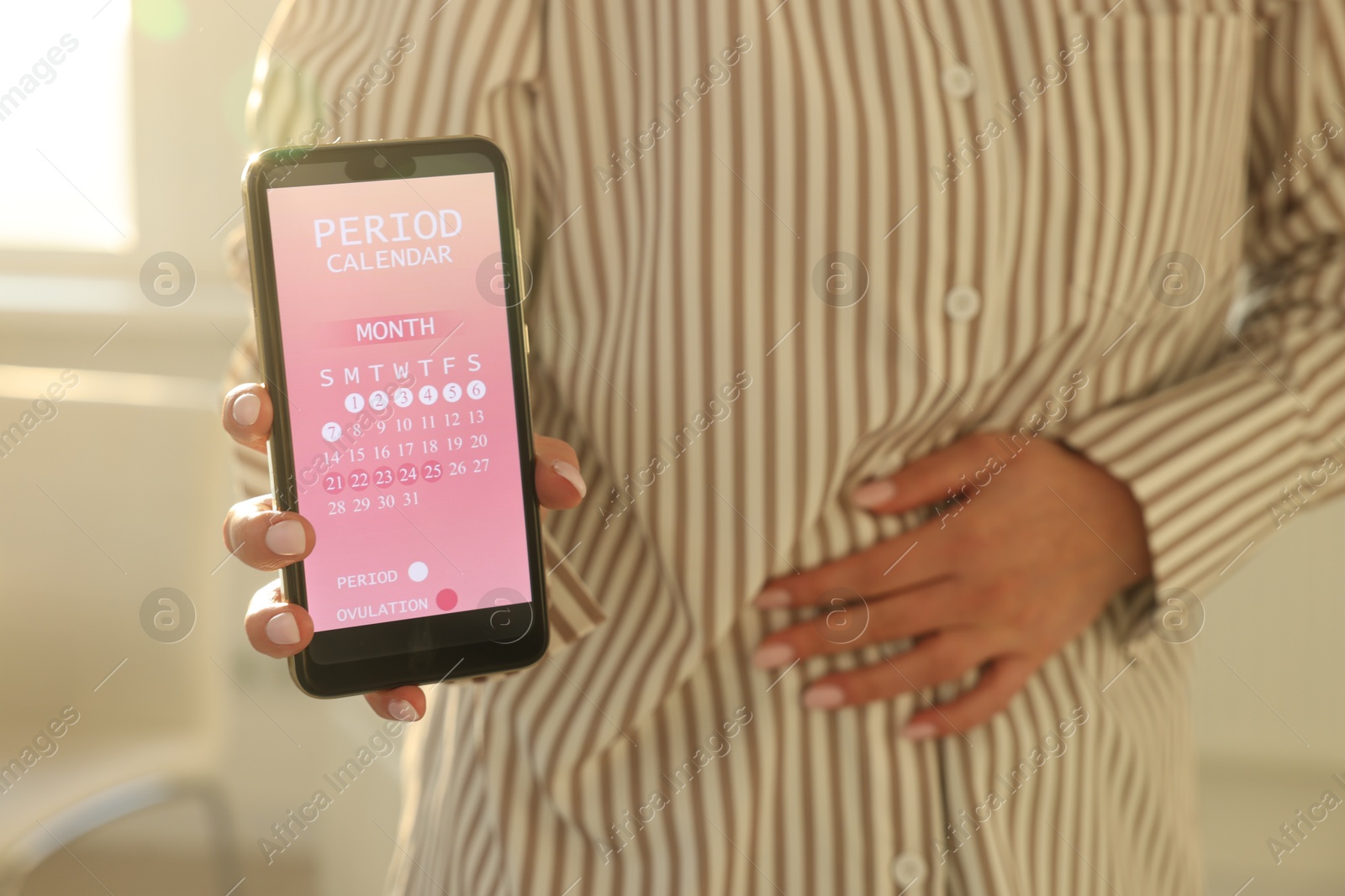 Photo of Menstruation. Woman holding smartphone with period calendar application and suffering from abdominal pain indoors, closeup