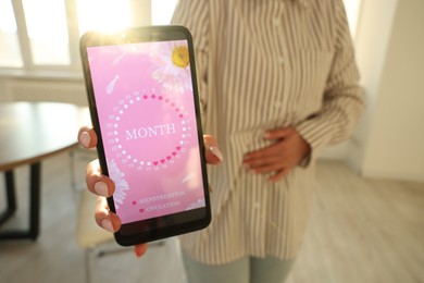 Photo of Menstruation. Woman holding smartphone with period calendar application and suffering from abdominal pain indoors, closeup