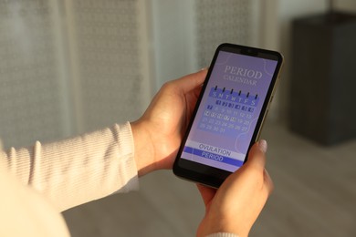 Photo of Menstruation. Woman using period calendar application on smartphone indoors, closeup