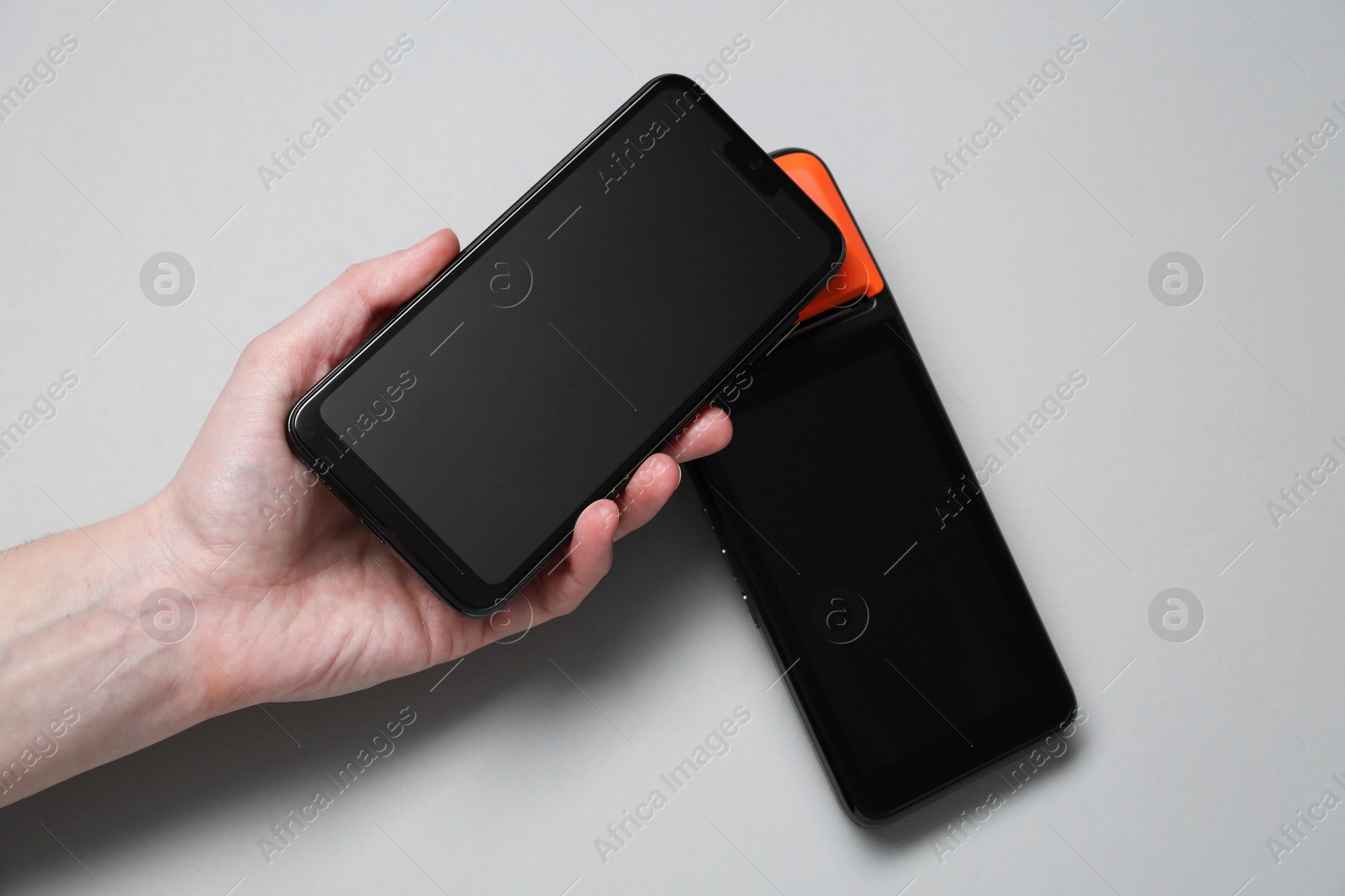 Photo of Woman with smartphone using payment terminal on grey background, top view