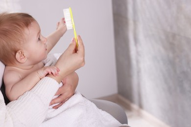 Photo of Woman brushing hair of her little baby indoors, closeup. Space for text