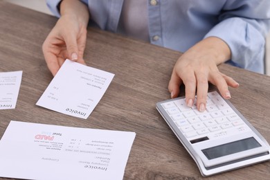 Photo of Paying bills. Woman with different invoices and calculator at wooden table indoors, closeup