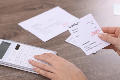 Photo of Paying bills. Woman with different invoices and calculator at wooden table indoors, closeup