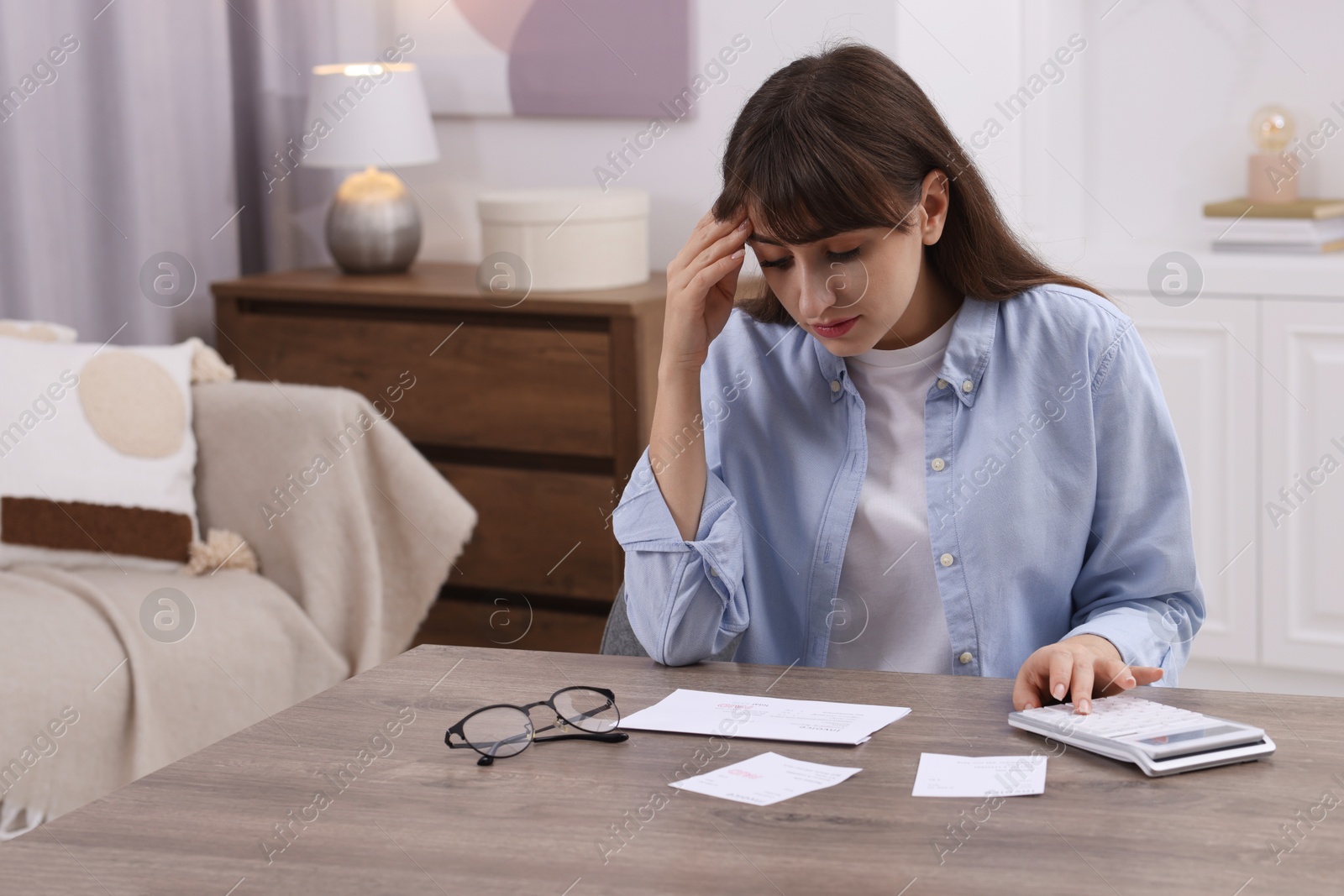 Photo of Paying bills. Upset woman with different invoices and calculator at wooden table indoors